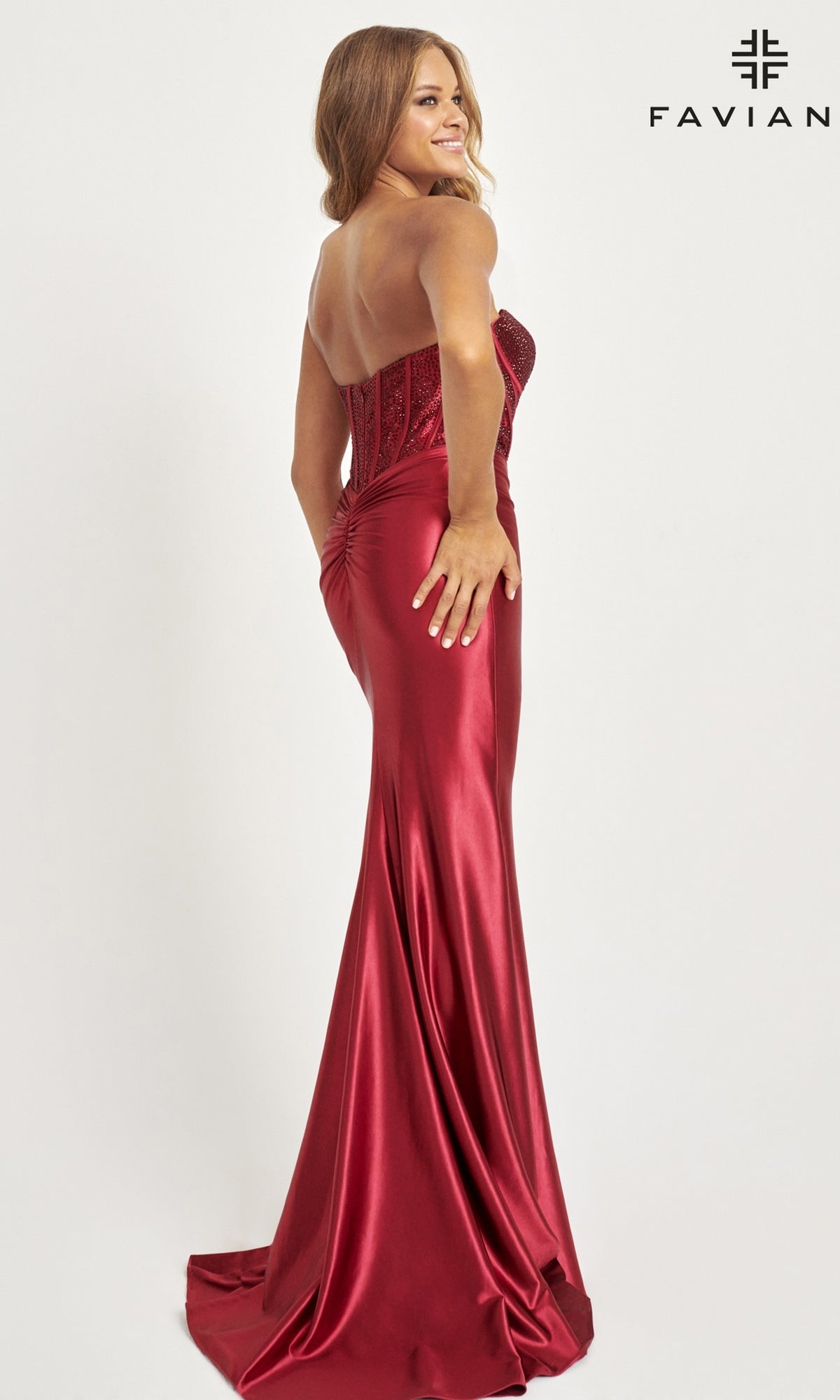 A woman models the Corset-Bodice Faviana Strapless Prom Gown 11006, with its fitted bodice and ruched back, posing gracefully against a plain white background.